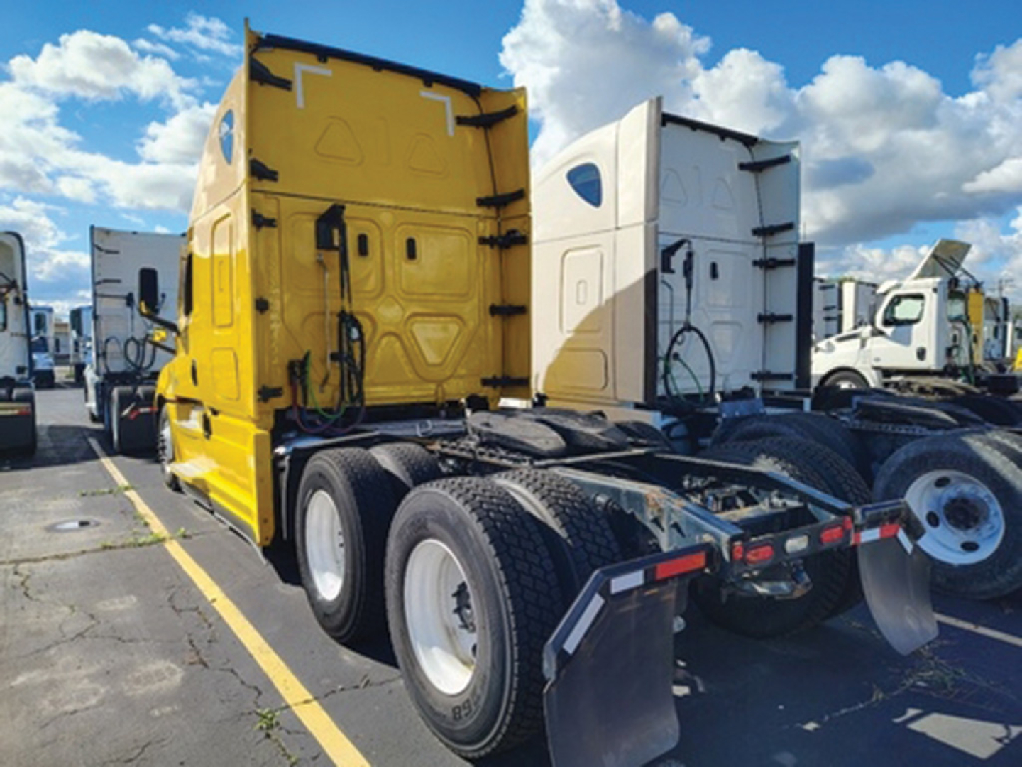 Freightliner Cascadia126 truck cab in yellow at a lot, rear view showing fifth-wheel hitch and dual rear axles, other trucks in background.