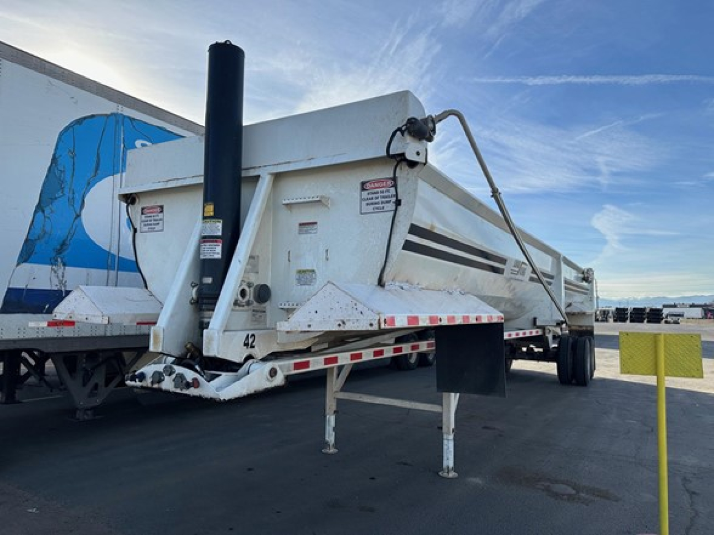 Load King rock end dump trailer showing white body with black stripe decals and support legs extended.