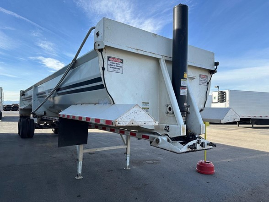 Load King rock end dump trailer showing hydraulic piston assembly and rear hitch with red safety cone.