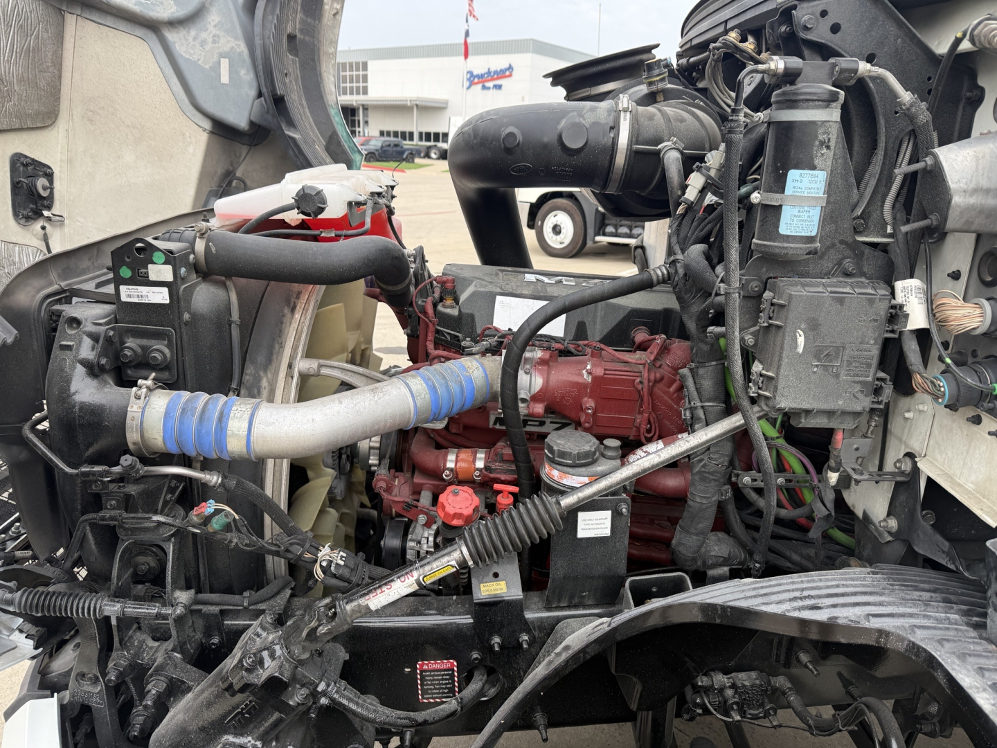 Mack AN42T engine bay showing red engine block, coolant hoses, and various labels in view through cab opening.