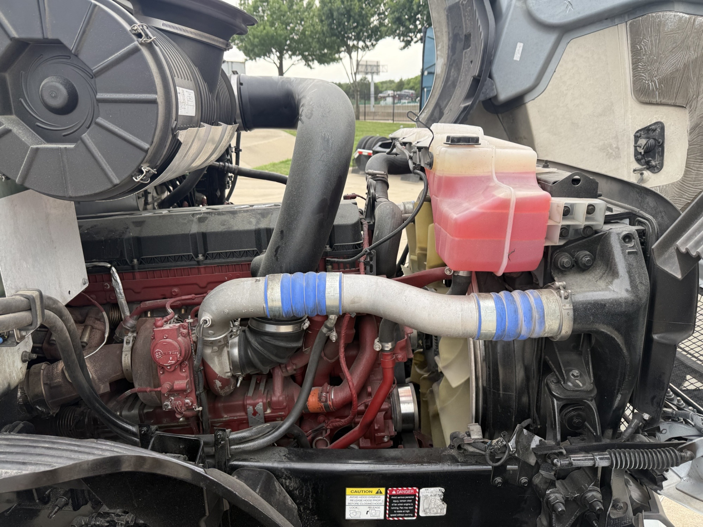 Tractor engine bay of a 2022 Mack AN42T daycab showing red engine block, coolant reservoir with pink/red fluid, blue hose clamps, and surrounding components.