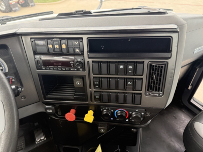 Dashboard and center console of 2022 Mack AN42T daycab showing radio, various control switches, air conditioning dials, and red/yellow power knobs.
