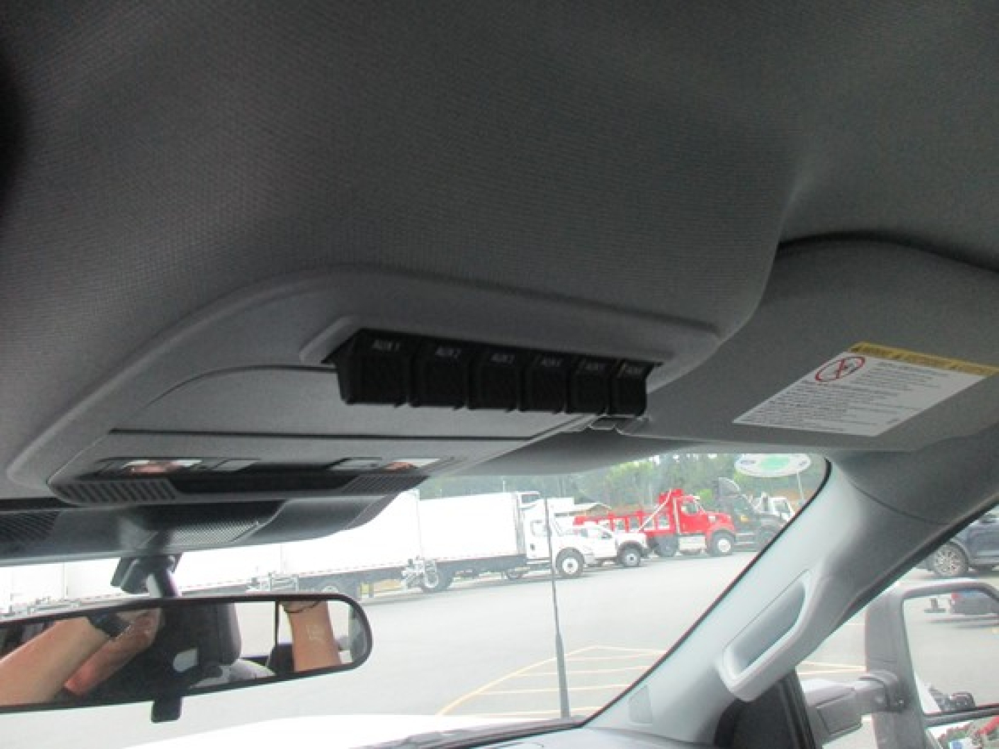Interior of a Ford F-550 cab showing overhead console and sun visor; windshield and side mirror visible. Text on stickers near sun visor and rearview mirror area partially legible.
