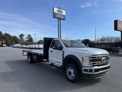 Ford F-550 flatbed truck in a dealership lot with white cab and flatbed; visible sign reads Ford and dealership information.