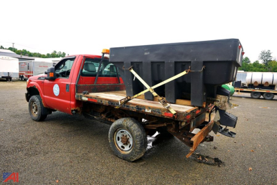 Ford F-350 Super Duty flatbed truck with a large rear dump hopper secured on the bed by straps, showing the tail and spare equipment.