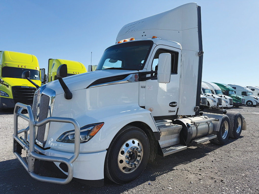 Truck cab and sleeper on a white Kenworth tractor showing front grille, bumper guard, side mirrors, and dual rear axles.