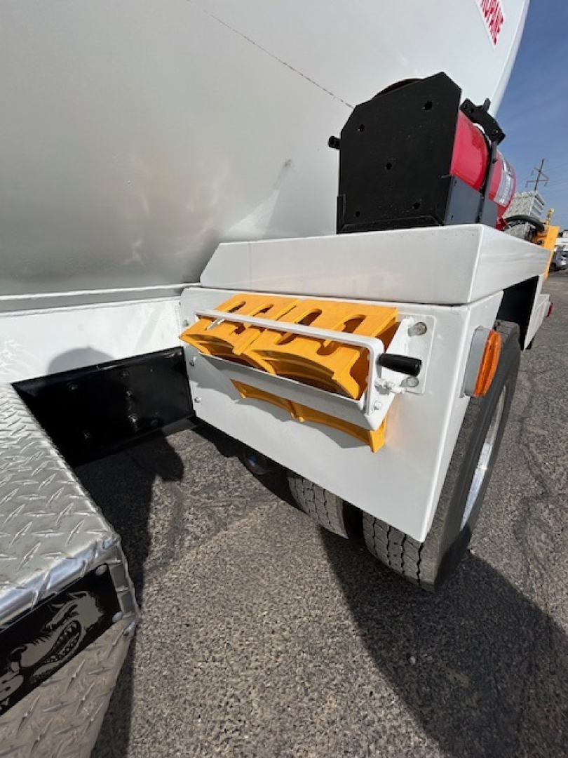 Wheel area of a Mack MD7 truck with a fuel or air tank and orange safety steps mounted on side, view of rear wheel and chassis.