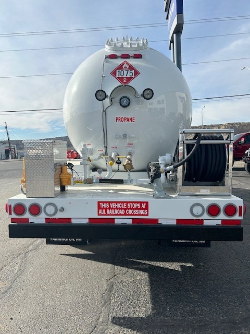 Tank trailer back view showing propane tank with hazard placard 1075 and rear hoses, valve assemblies, and bumper with warning text.