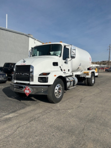 White Mack MD7 concrete mixer truck shown from front-left angle with tank behind cab, DOT placard on bumper, clear sky.