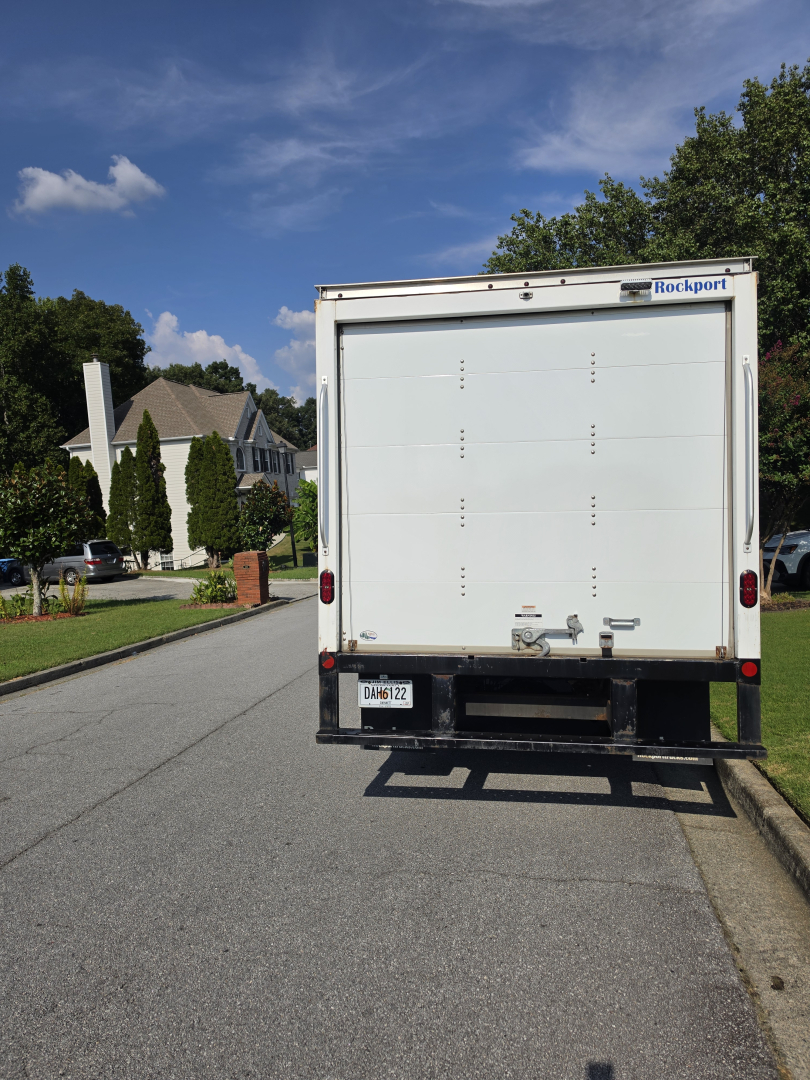 Rear view of a white box truck with Rockport label, liftgate, and bumper. License plate visible.