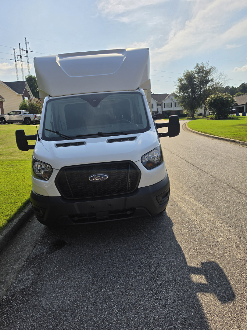 Front view of a white Ford Transit 350 HD box truck with a highroof, large grille, and black bumper. Side mirrors extended.