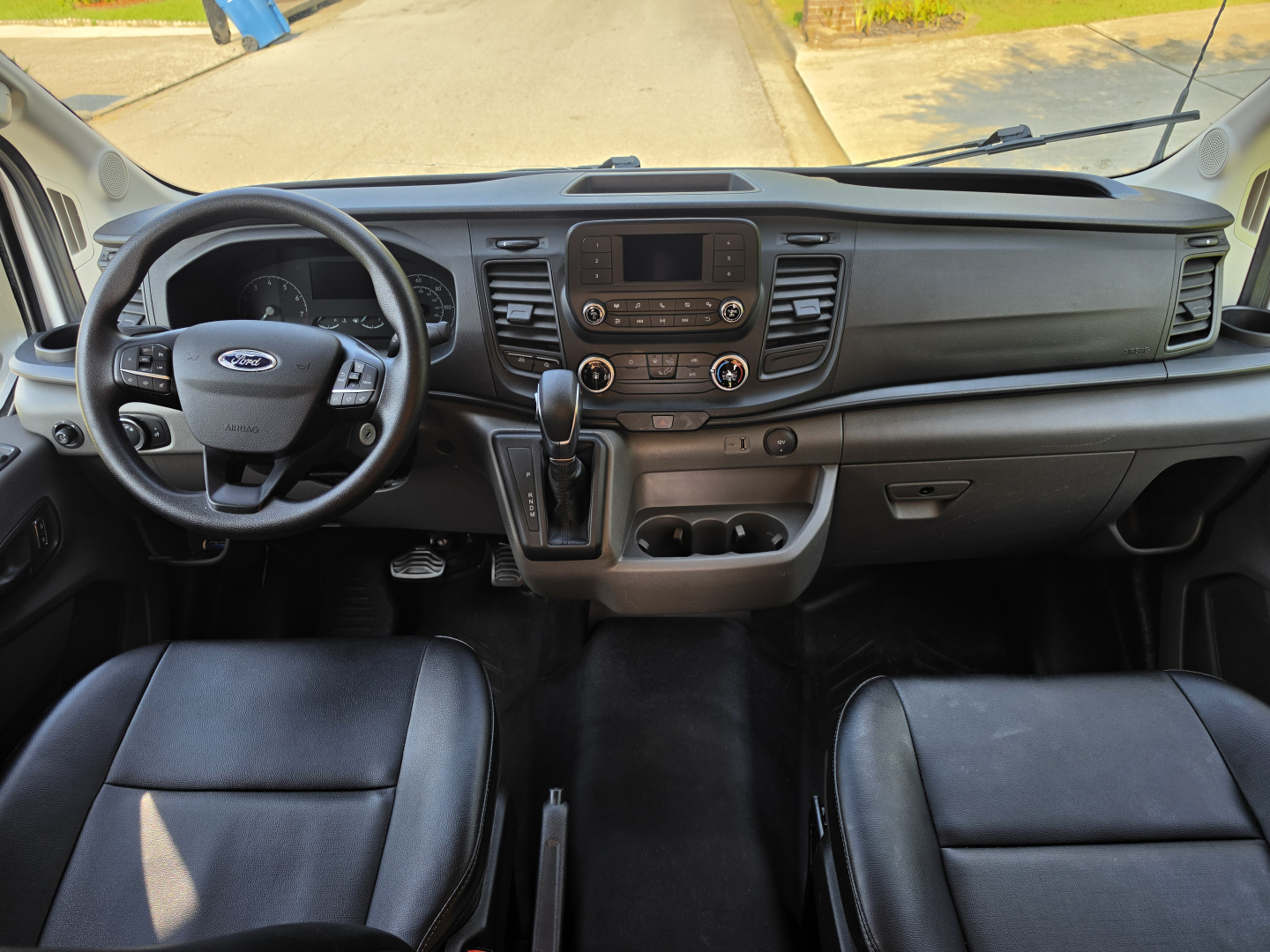 Ford Transit 350 HD interior dashboard and steering wheel, center console with touchscreen display, gear shifter, and cup holders.