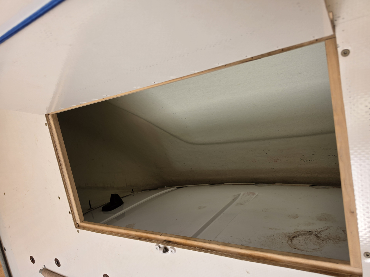 Truck interior side opening showing cargo area with white floor and light green walls, wooden frame around hatch, some dirt and marks.
