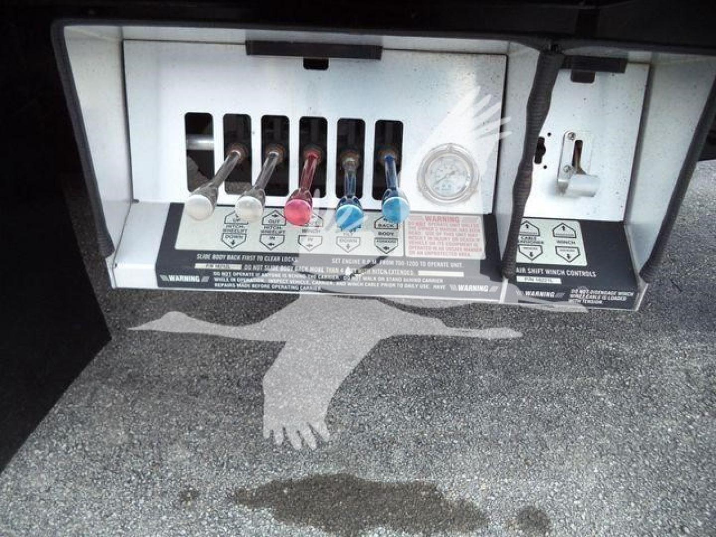 Truck bay with control levers and labels; visible text includes various warning labels and color-coded levers (red, blue, black) for fluid control in a rollback truck.