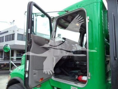Truck cab interior with open door of a green 2018 Peterbilt 348 rollback truck. Visible are driver seat, steering wheel, dashboard, and a red fire extinguisher under the seat.