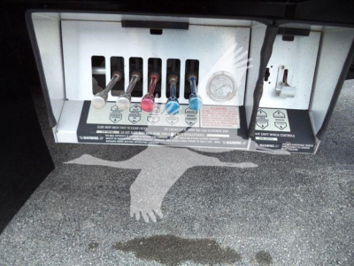 Truck bay with control levers and labels; visible text includes various warning labels and color-coded levers (red, blue, black) for fluid control in a rollback truck.