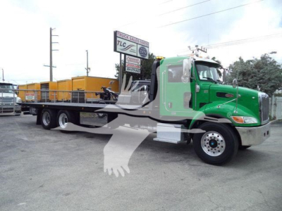Peterbilt 348 rollback truck in green with flatbed and yellow cargo in background.