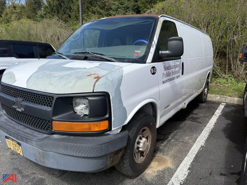 Chevrolet Express 3500 cargo van from the front-left view with faded primer and repair patches on the hood, black front bumper, orange turn signal, and company logo on the side.
