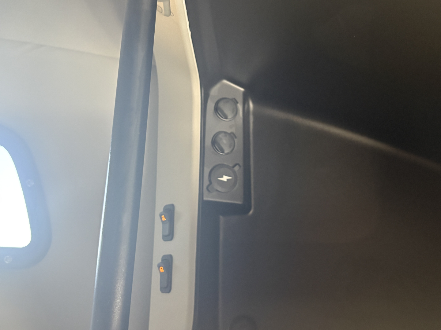 Panel in cab showing two small orange indicators and a circular power/socket symbol on a black surface.
