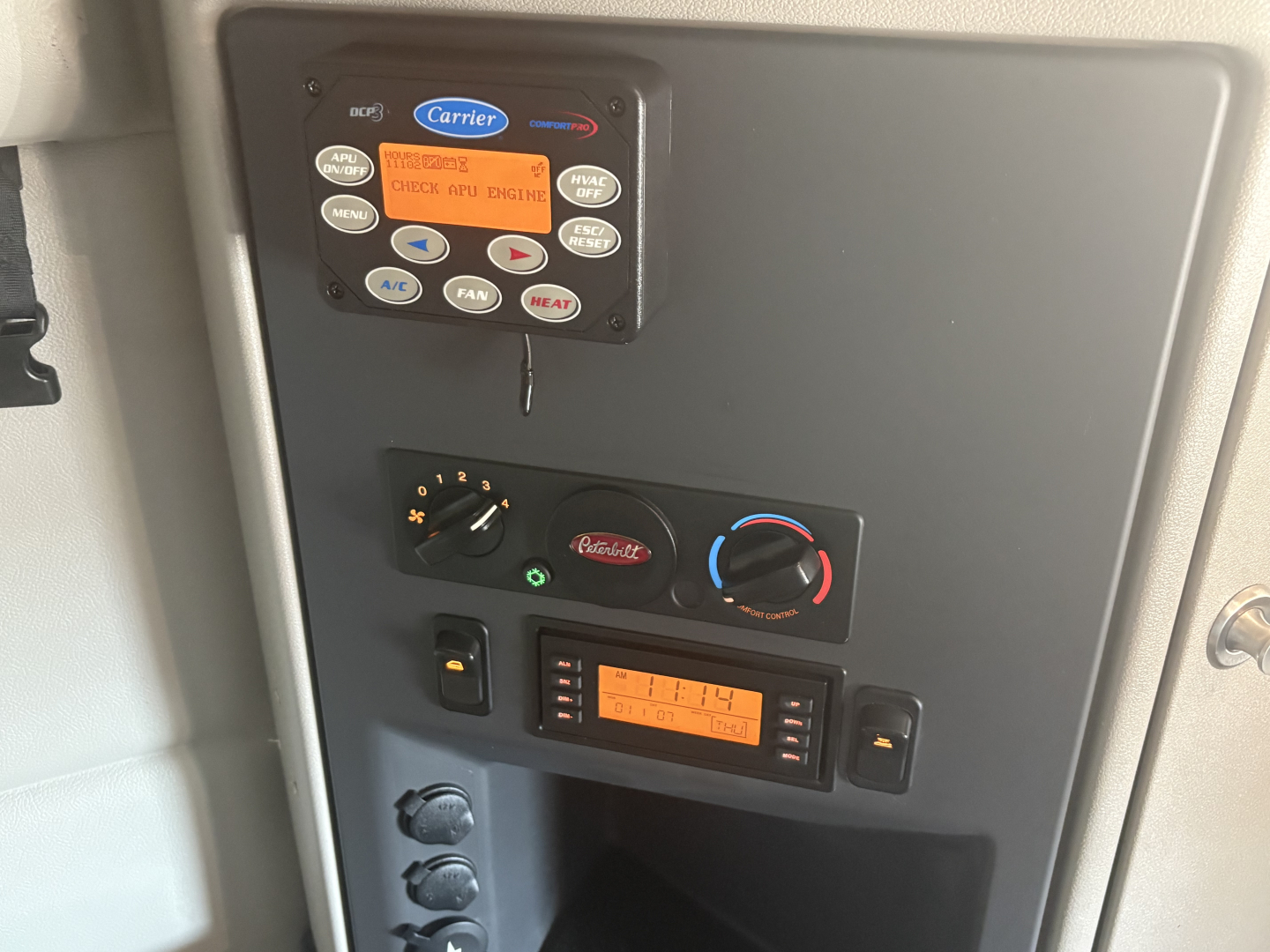 Truck cab control panel with digital display and climate controls. Visible text includes Carrier brand labels, 'CHECK AIR ENGINE' on orange screen, various buttons around.