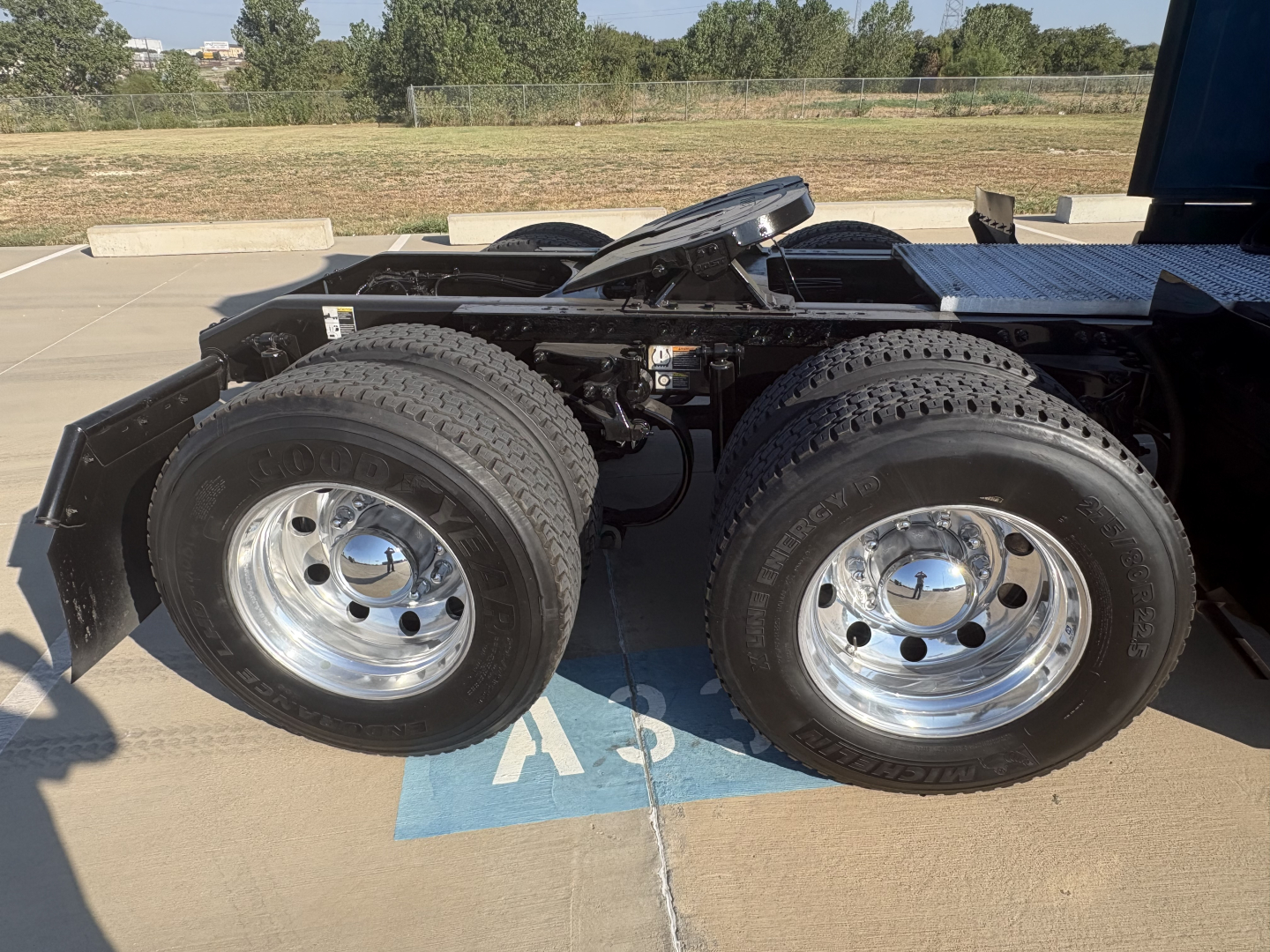 Peterbilt 579 truck rear showing dual rear axles with dual tires and chrome wheels, fuel tank and chassis visible in a parking lot.