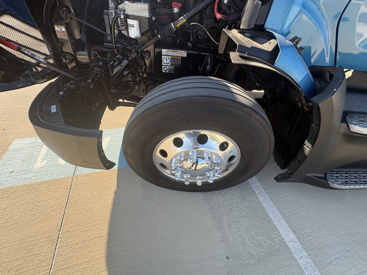 Peterbilt 579 truck front wheel and engine bay components showing front tire and chrome hubcap.