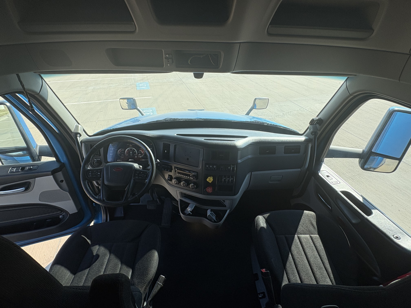 Peterbilt 579 interior dashboard view from driver seat showing steering wheel, instrument cluster, center console, and driver and passenger seats.