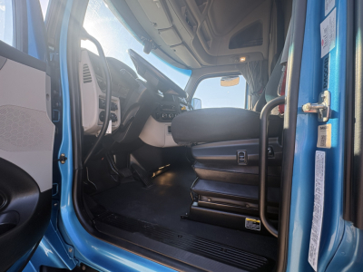 Peterbilt 579 cab interior view from open driver door showing steering wheel, dashboard, driver seat, and entry step in blue exterior.