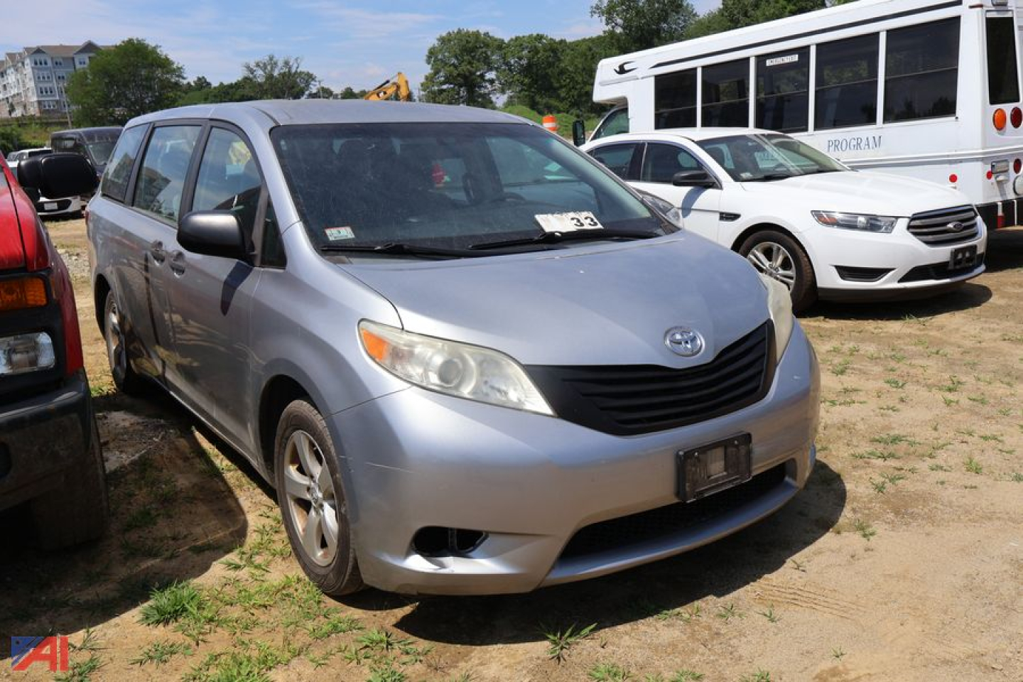 Front-left view of a light blue 2016 Toyota Sienna minivan parked on dirt with other vehicles nearby.