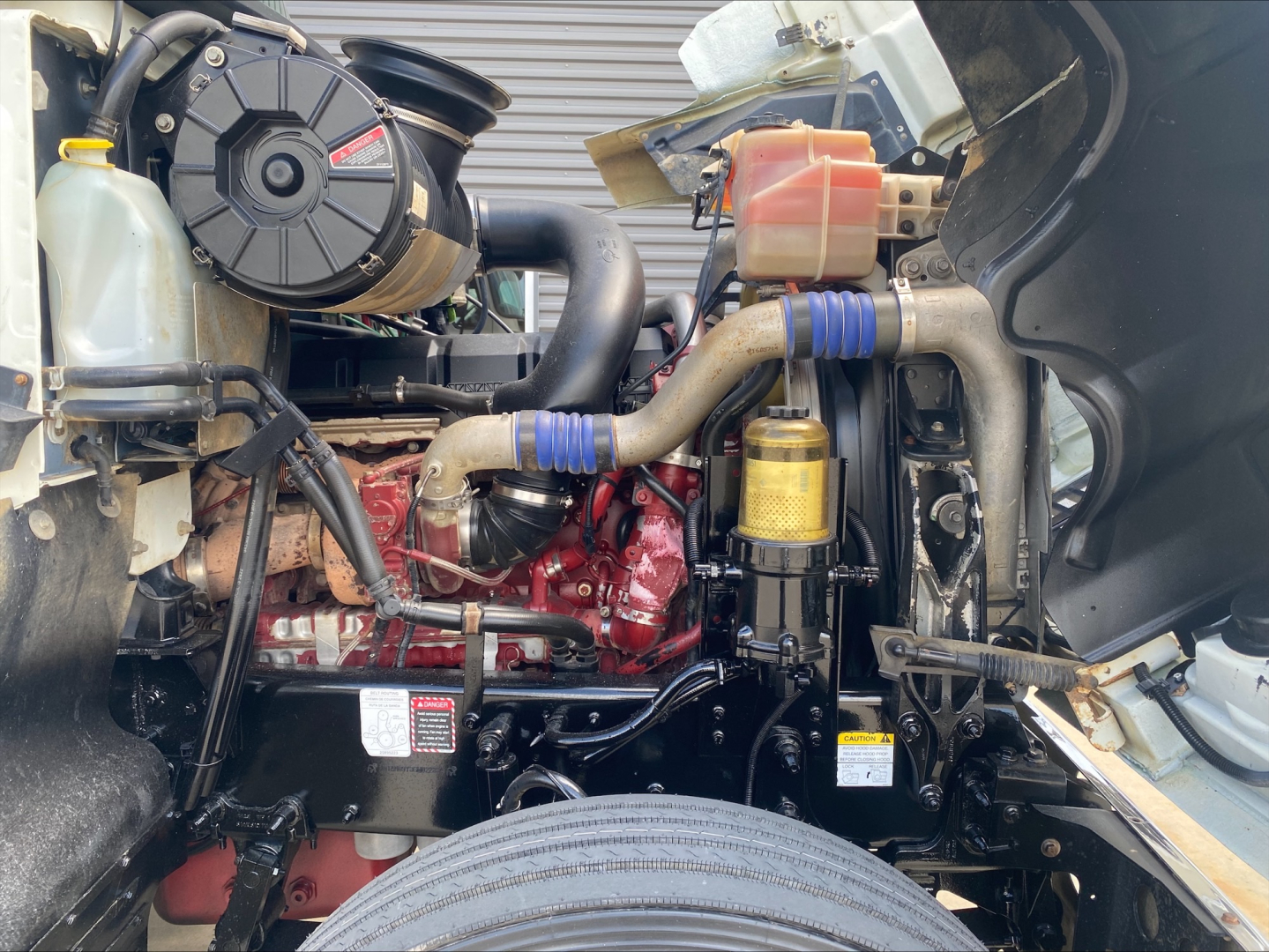 Truck engine bay of a 2020 Mack AN64T70 showing engine, coolant reservoir, hoses, and various components.