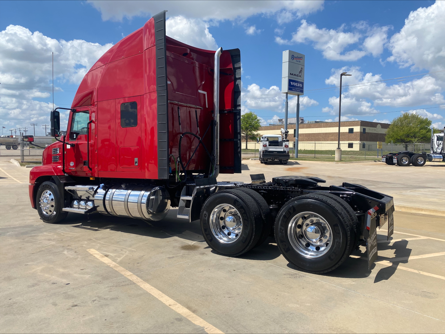 Mack AN64T70 conventional sleeper tractor in red with tandem rear axles and chrome fuel tanks, side view in a truck lot.