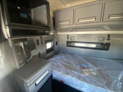 Truck cab interior with bunk area and storage cabinets. Visible text includes 'MACK' badge on bunk door and plastic-wrapped mattress. No other legible text visible.