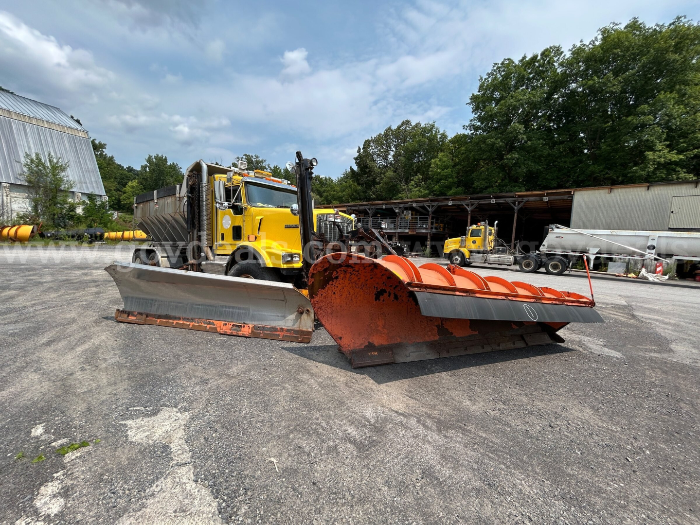 Kenworth T800 plow truck with large orange snow plow blades in an outdoor lot, yellow truck cab in background, stock number 3691-17 listed as used.