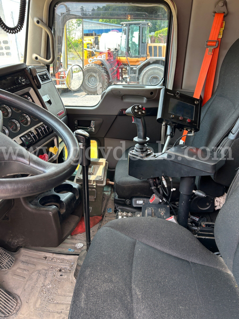 Cab interior of a Kenworth T800 showing steering wheel, gear shifter, control panel, and operator seat with mount for display; external equipment visible through window.