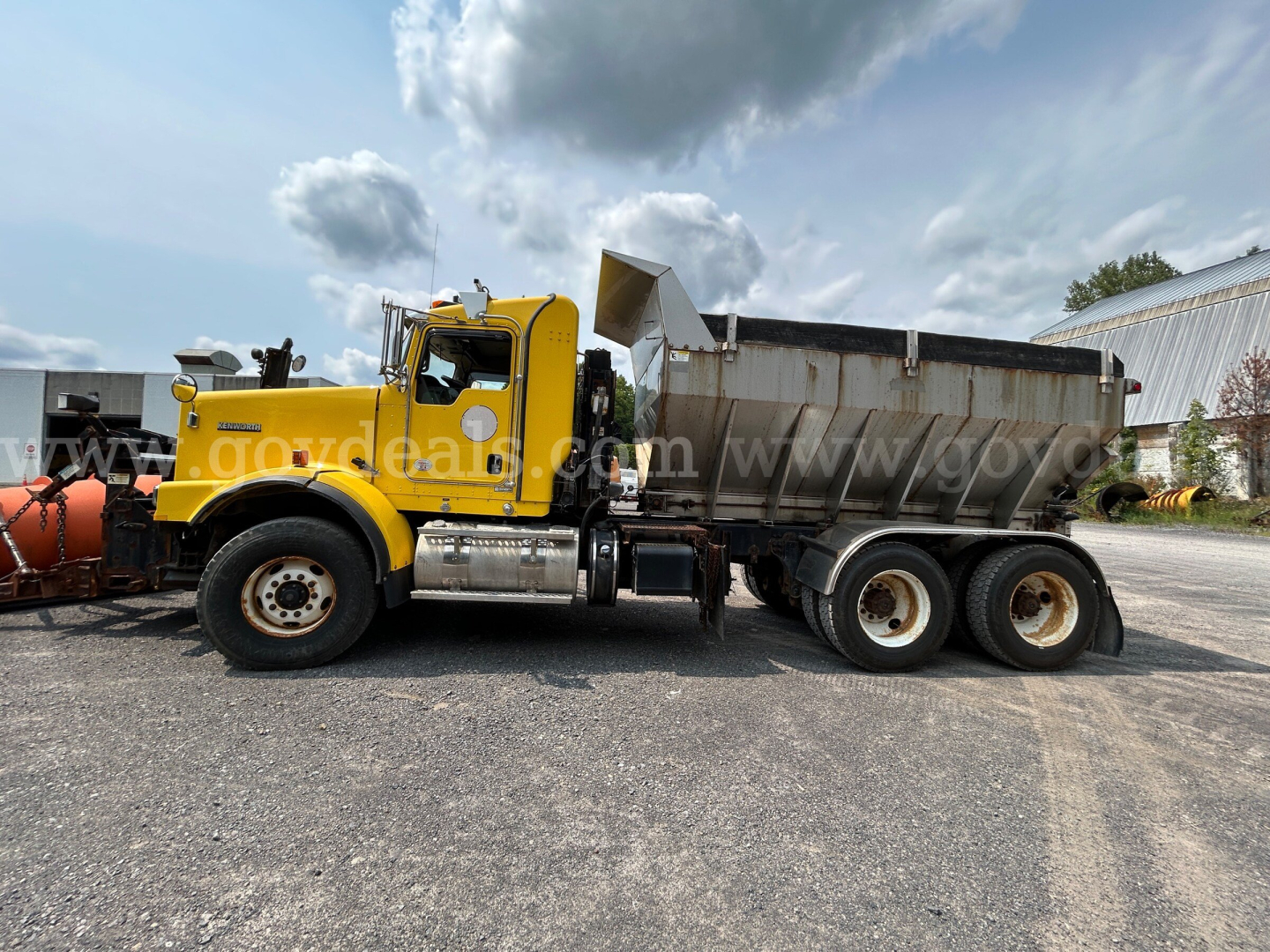 Kenworth T800 dump truck with yellow cab and gray dump bed, side view showing dual rear axles and wheel rims.