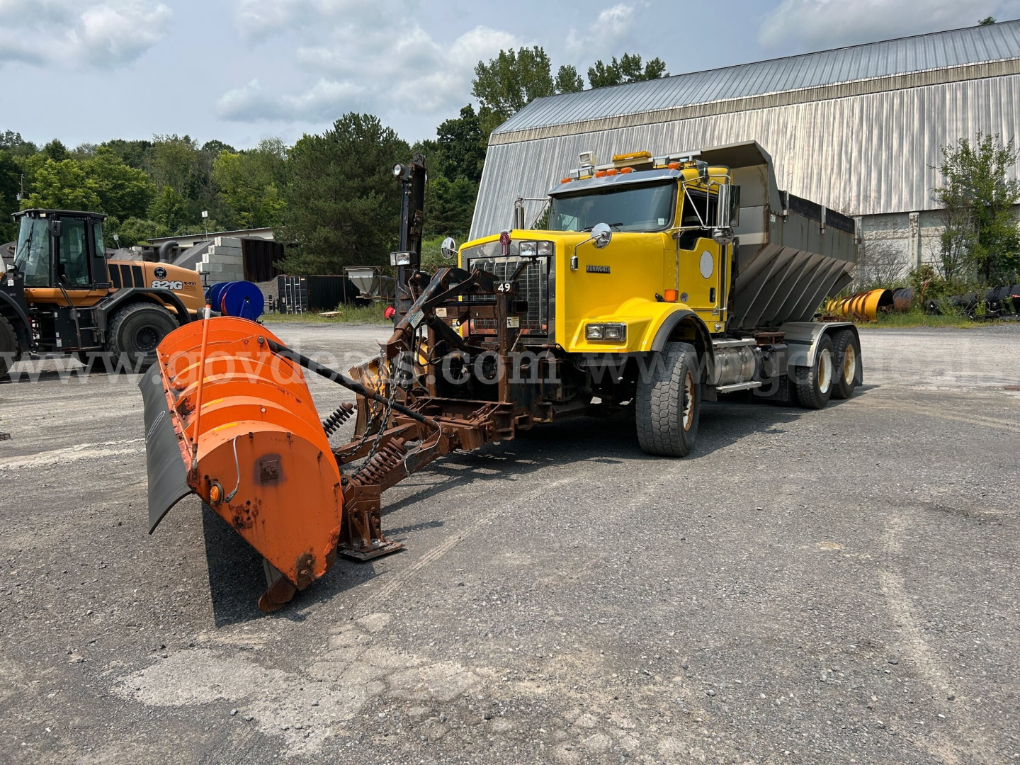 Kenworth T800 plow truck with large orange snow plow attachment in foreground, yellow cab, and dump body in background.
