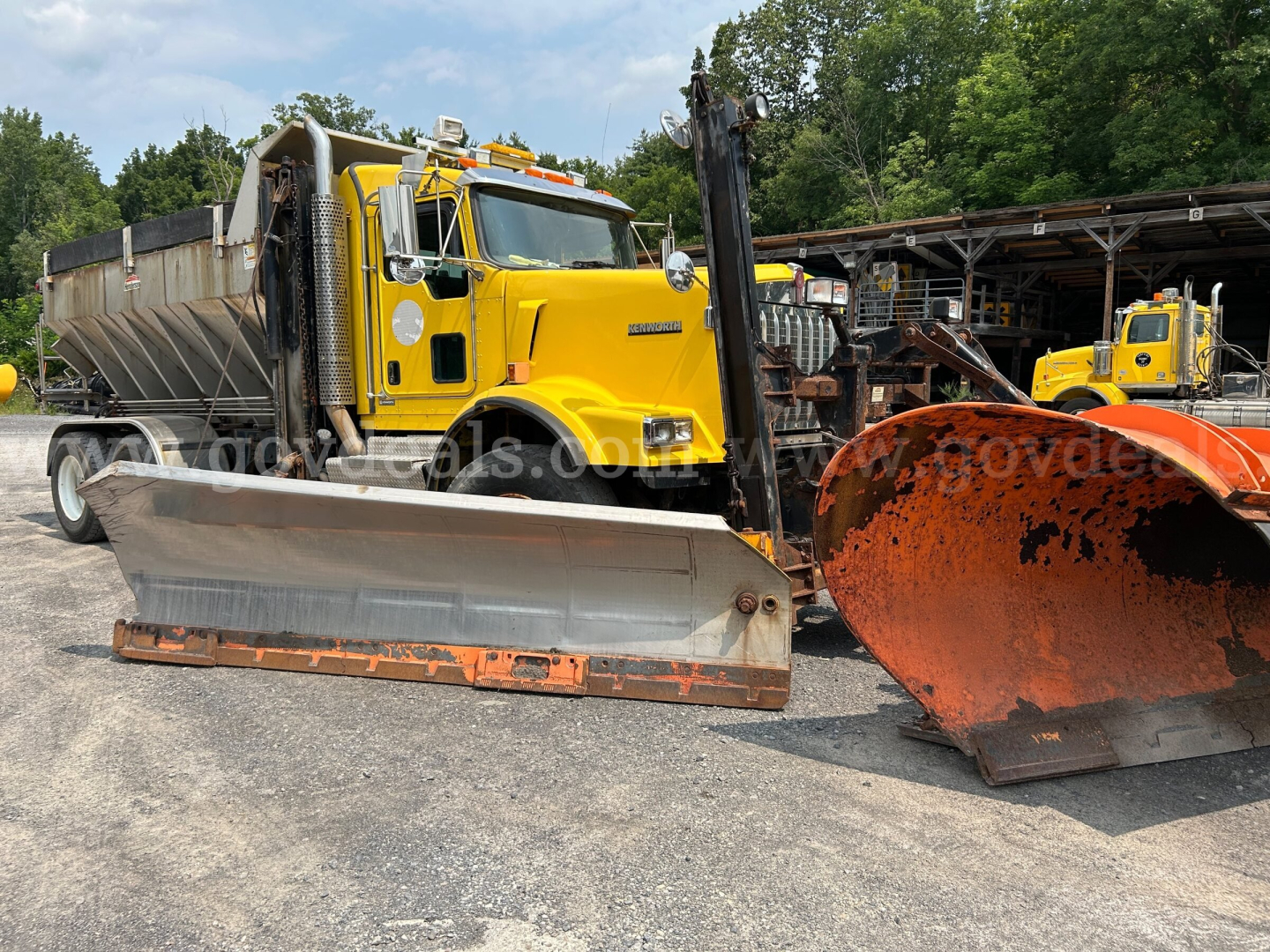 Kenworth T800 snow plow truck in yellow, with large front plow and orange snow blade in foreground.