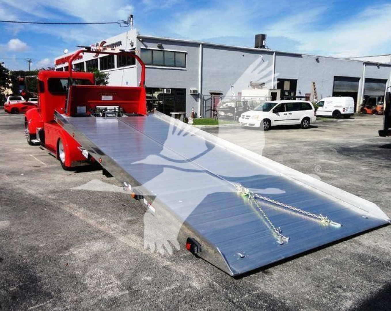 Peterbilt 337 rollback tow truck with a long aluminum tilt bed, red cab, in a dealership lot.