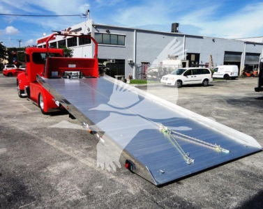 Peterbilt 337 rollback tow truck with a long aluminum tilt bed, red cab, in a dealership lot.