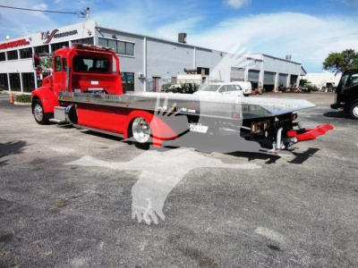 Peterbilt 337 rollback truck showing red cab and flatbed with equipment in rear, dealership lot in background.