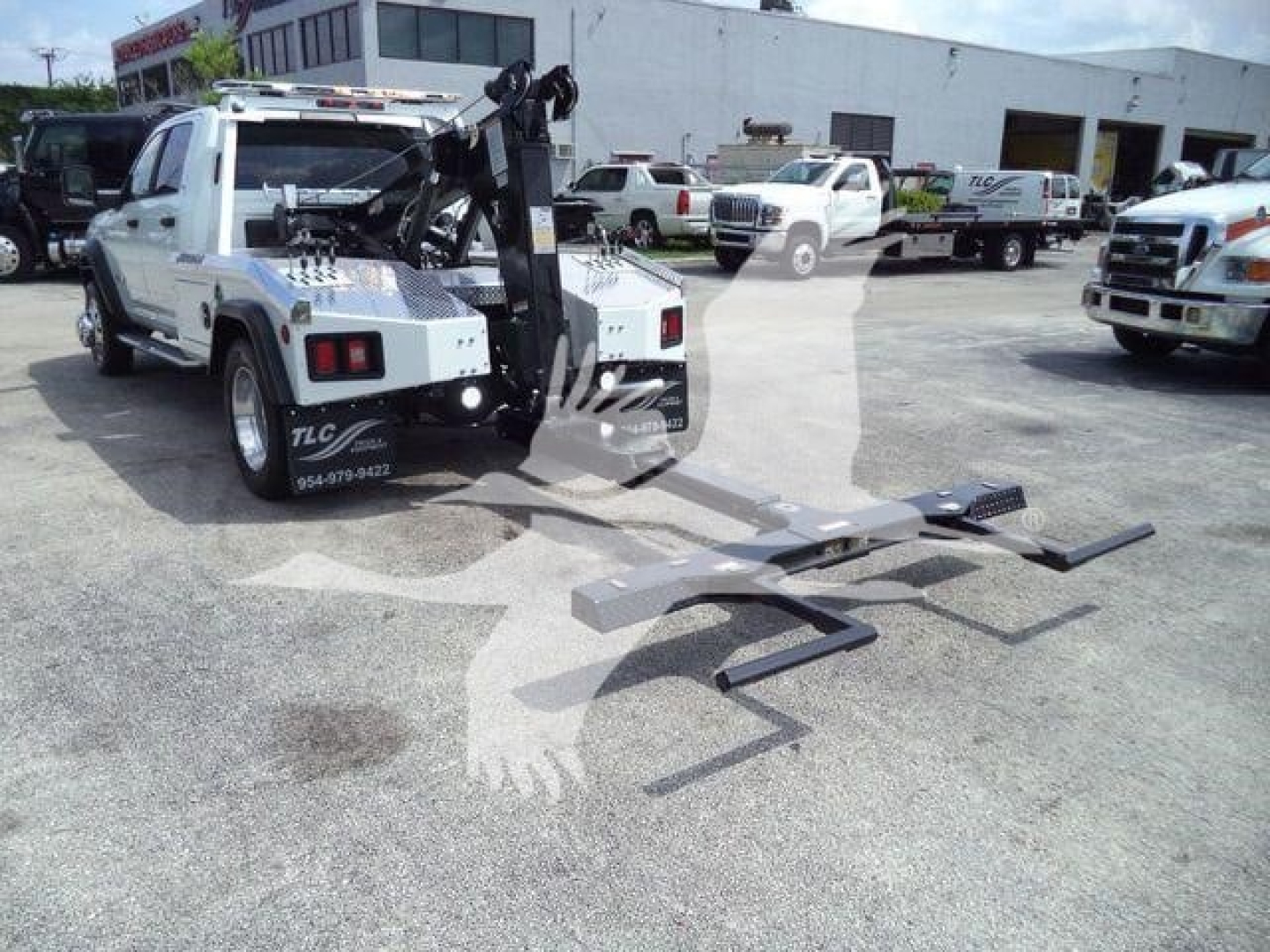 Ram 5500 tow truck with front-mounted winch and flatbed extension in a dealership lot, white body, multiple trucks in background.