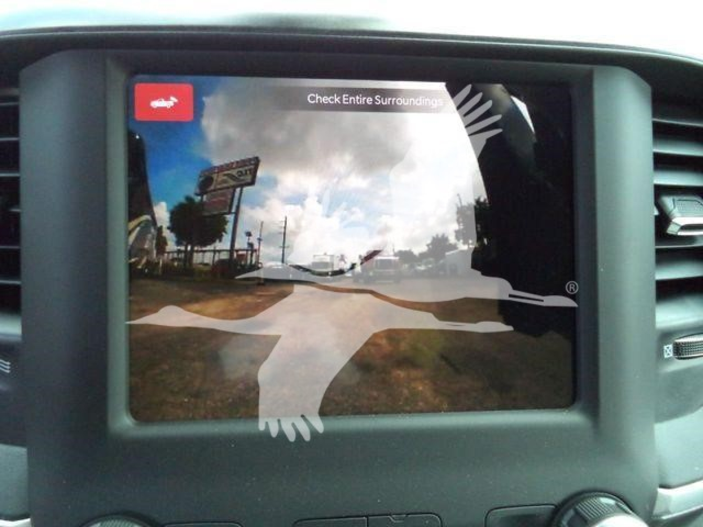 Truck dashboard screen showing rearview camera image with warning text 'Check Entire Surrounding' and a silhouette overlay.