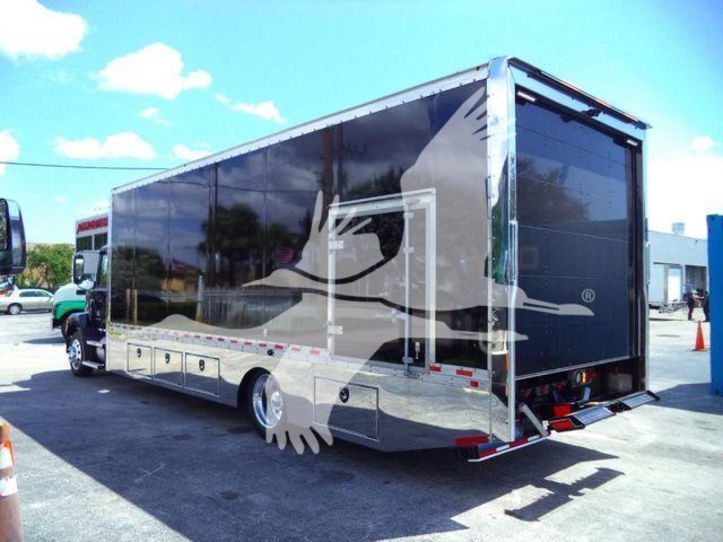 Truck body rear view showing a black glossy enclosed rollback/box with reflective chrome detailing and storage compartments along the lower side, Mack Md6 stock number 26FTMD6TOWBOX.
