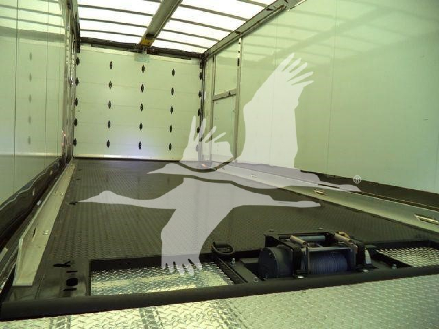 Interior of a Mack MD6 rollback truck cargo area with metal flooring and tiedown points visible, empty load space.