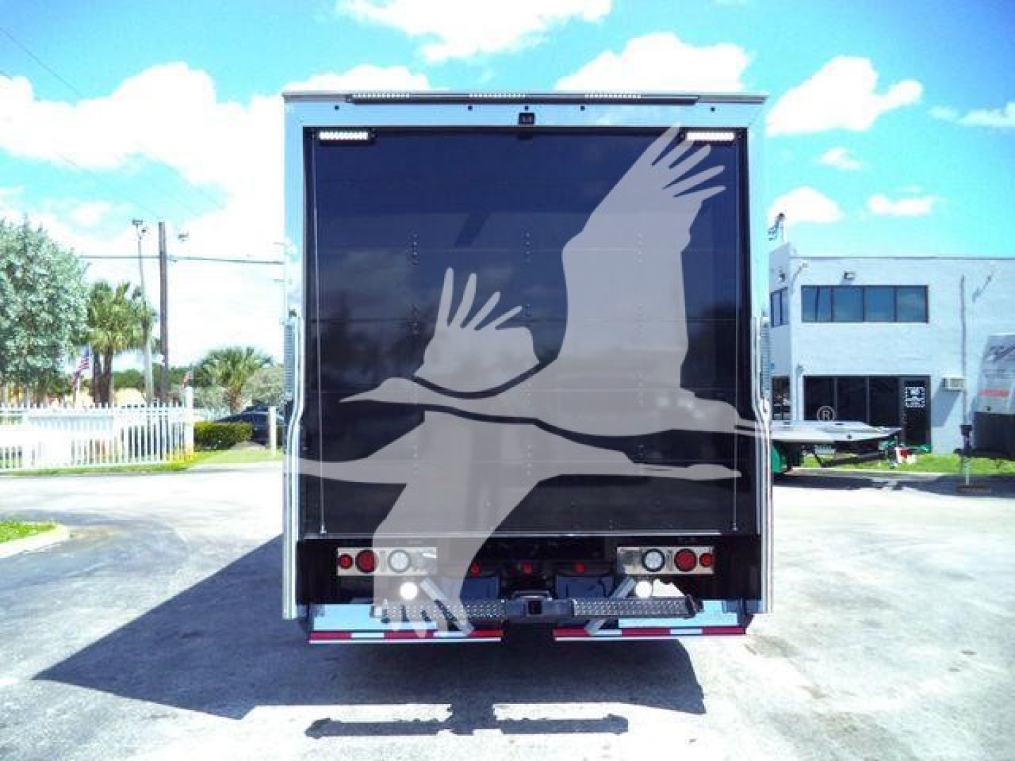 Rear view of a Mack MD6 rollback truck with a large graphic of birds on the cargo door; trailer lights and bumper visible.