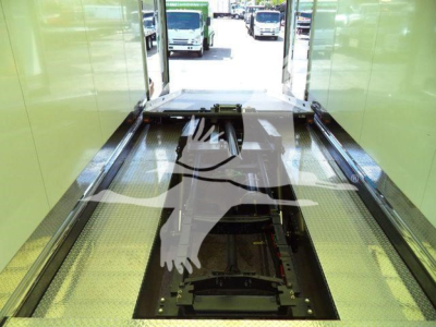 MD6 truck inside a green rollback bay, viewing the chassis/drive area with open floor pit for wheel lift.
