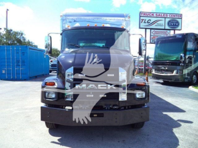 Front view of a 2026 Mack MD6 rollback truck with a large black bumper; visible logos and text on grille area; background includes other trucks and a sign.