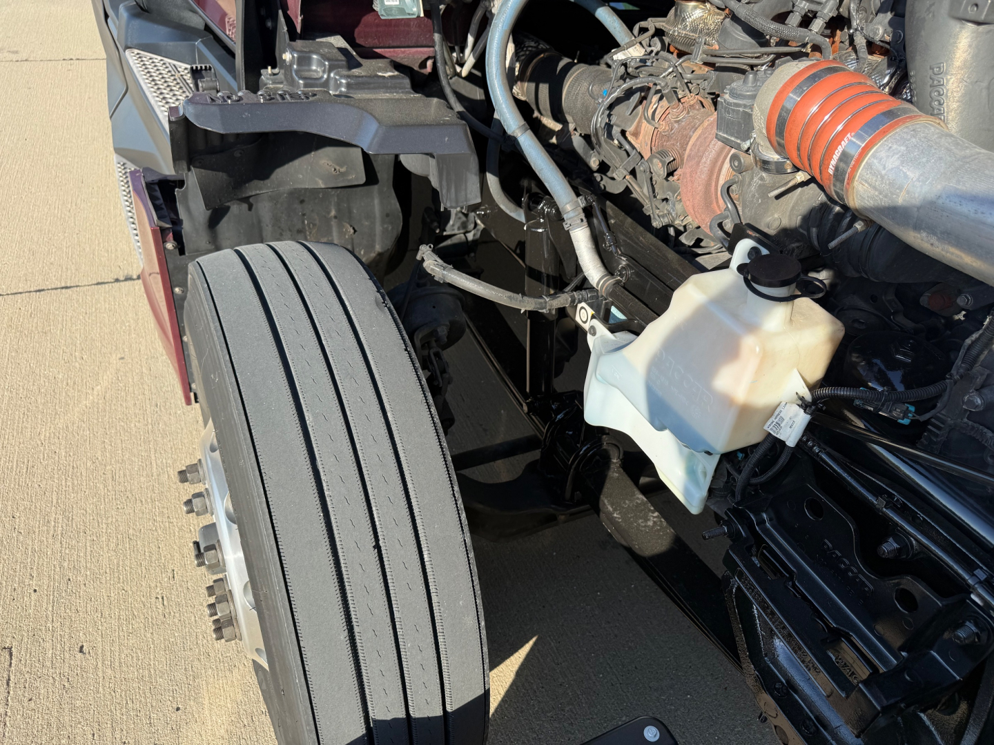 Kenworth T680 engine bay and front wheel with visible coolant reservoir and intake hose in the engine bay.