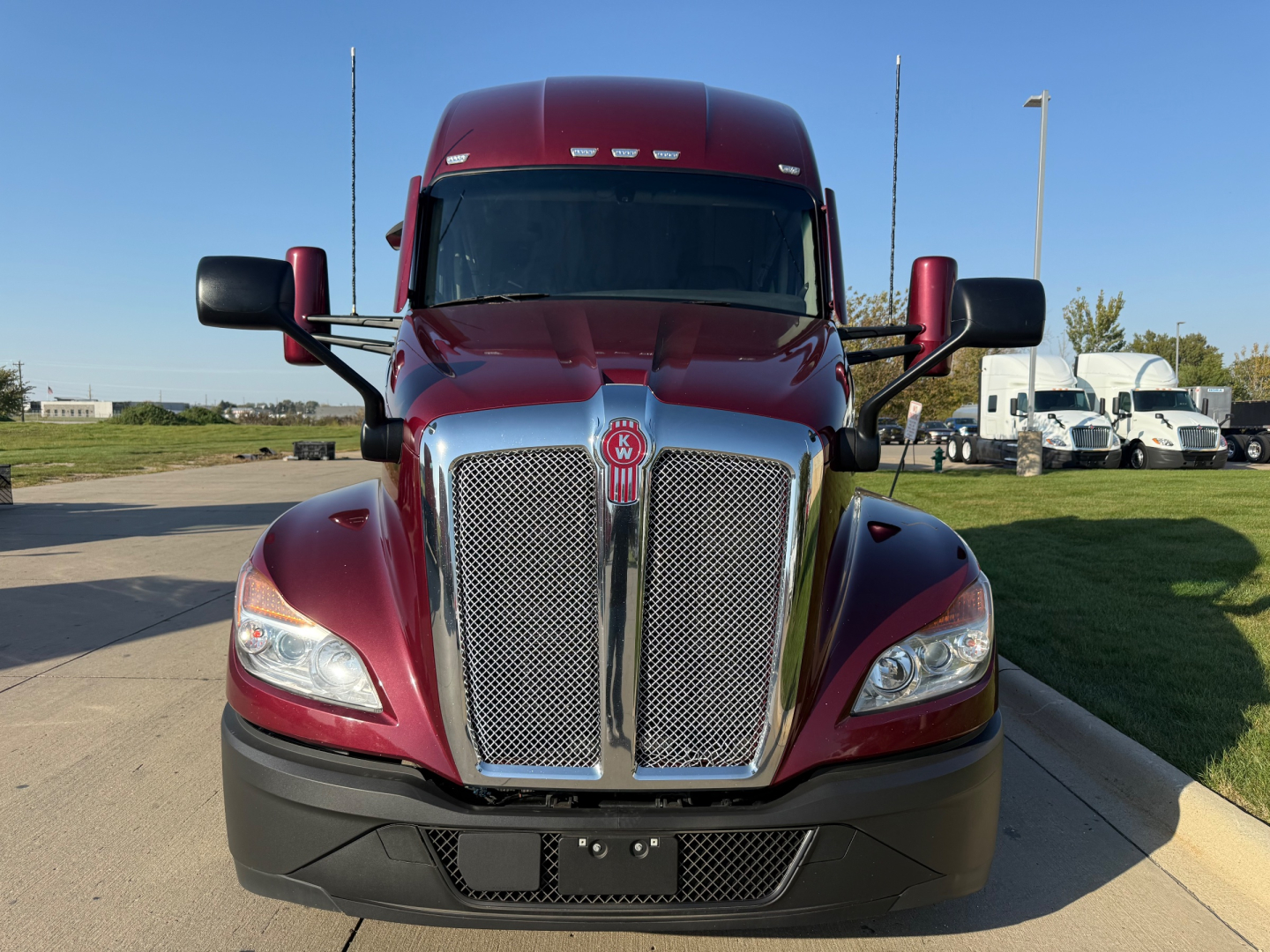 Kenworth T680 front view showing chrome grille, red cab, black bumper, and side mirrors.