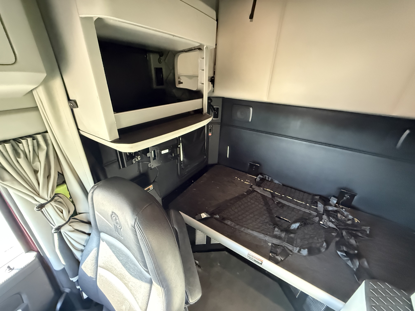 Kenworth T680 sleeper cab interior showing bunk area and storage shelf with harnesses and seating in front.